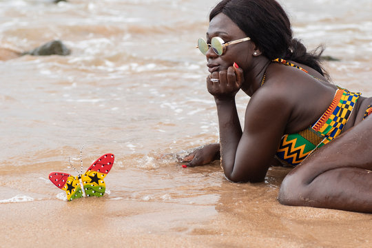 Ghana woman lies on the beach with a butterfly painted as the flag of Ghana.