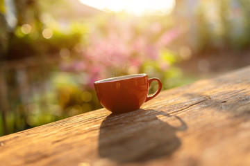 Red coffee cup on wooden table morning nature light in garden concept