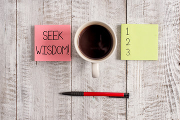 Writing note showing Seek Wisdom. Business concept for ability to think act using knowledge experience understanding Stationary placed next to a cup of black coffee above the wooden table