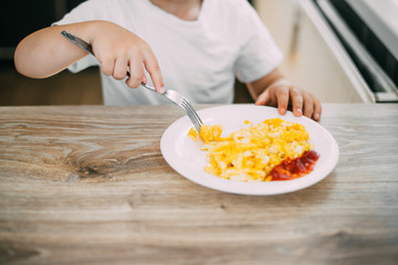 a child in a t-shirt in the kitchen eating an omelet with a fork is very tasty
