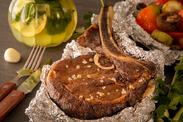 Meat steak baked in foil and baked vegetables with a steamed mug of mint drink on a wooden table. Close-up