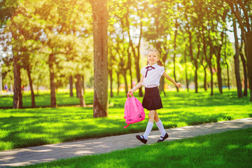 Fototapeta premium Portrait of happy Caucasian young smiling girl wearing school backpack outside the primary school. schoolgirl, elementary school student runs jumping from school, graduation, summer holidays.