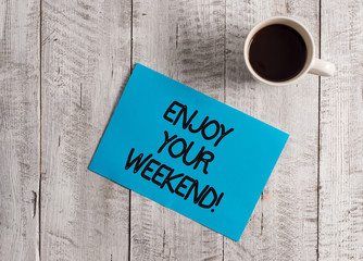 Text sign showing Enjoy Your Weekend. Business photo showcasing wishing someone that something nice will happen at holiday Pastel Colour paper placed next to a cup of coffee above the wooden table