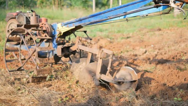 Old man using a small tractor to plow the farm to adjust the soil for planting.