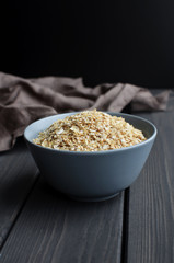 Rolled oats in ceramic bowl on dark wooden table with texture