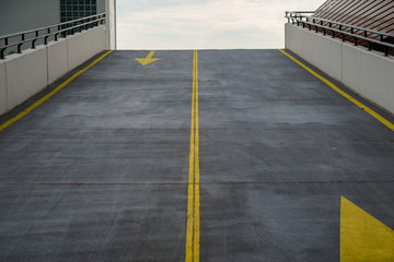 Asphalt road, driveway to multi-storey parking lot, garage with grunge surface texture and contrasting yellow color of traffic markings, arrows. View from bottom.