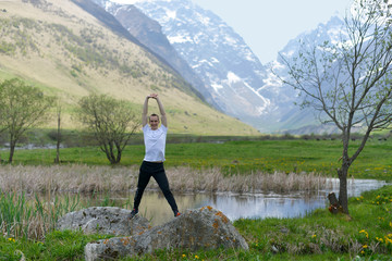 Naklejka premium A young sports man stands near a cold mountain lake in the warm spring against the background of snow rocks.