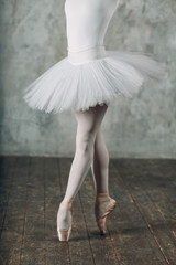 Ballerina in ballroom. Young woman ballet dancer, legs and pointe shoes and white tutu. Ballet concept.