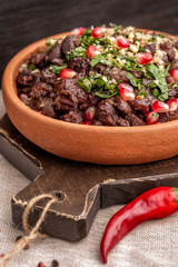 Kuchmachi Traditional Georgian dish of chicken giblets. A large portion served on a clay plate in a rustic style. Served with pomegranate seeds and greens. Close up and vertical view.