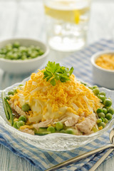 Chicken salad with mayonnaise. With a side dish of cucumber, green peas and boiled egg yolk. Served portion in glassware. Close up and vertical view.