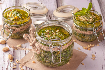 Green pesto sauce. Classic Italian sauce. Preservation in a glass jar. Three jars of sauce decorated in a rustic style. Close up and horizontal orientation.