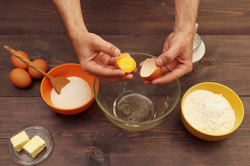 Chef hands break an egg over a bowl on a wooden table.