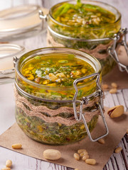 Green pesto sauce. Classic Italian sauce. Preservation in a glass jar. Two jars of sauce decorated in a rustic style.  Close up and vertical orientation.