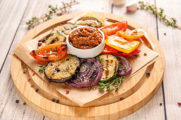 Grilled vegetables with fresh spic greens and pesto sauce of red tomatoes. Garnish for ketogenic and paleo diets. Large portion on a wooden plate in a rustic style.