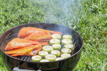 Picnic outdoors in the summer. Cooking on a round grill fish sea bass and zucchini slices