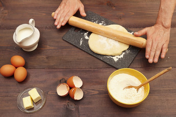 Chef rolling dough with rolling pin on the board on a rustic table.
