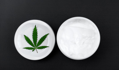 Close up of jar of cream from biological and ecological plants of hemp vegetable pharmaceutical oil CBD with green cannabis leaf with copy space