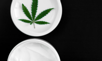 Close up of jar of cream from biological and ecological plants of hemp vegetable pharmaceutical oil CBD with green cannabis leaf with copy space