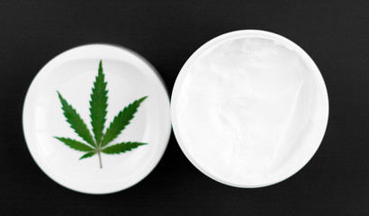 Close up of jar of cream from biological and ecological plants of hemp vegetable pharmaceutical oil CBD with green cannabis leaf with copy space