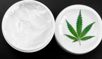 Close up of jar of cream from biological and ecological plants of hemp vegetable pharmaceutical oil CBD with green cannabis leaf with copy space