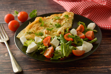 Traditional breakfast - egg omelette with cherry tomato, mozzarella and green salad. Wooden background.