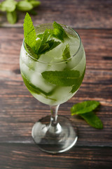 Summer cocktail drink in wine glass. Refreshing drink with mint leaves, gin tonic, syrop. Wooden background.