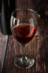 Glass of red wine over rustic, wooden textured table. Dark photo.