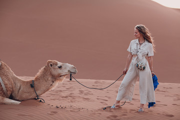 Caucasian young woman in linen clothes with camel in desert