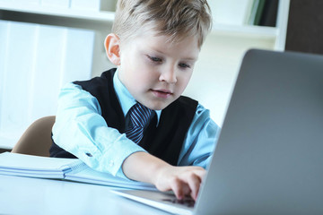 Small cute boy in business suit with a tie works at computer at office.