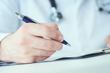 Male physician medicine doctor or pharmacist writing prescription on special form sitting at worktable. Medical care, pharmacy or health insurance concept.