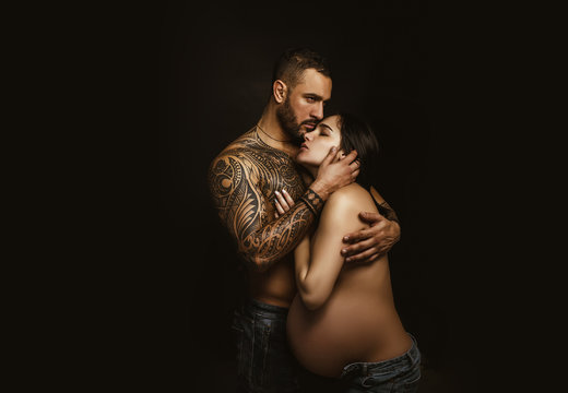 Couple in love pregnant cuddling, waiting for baby. Real romantic passionate moment. Bearded man with tattoo clasping beautiful girlfriend. Emotive of sexy couple.