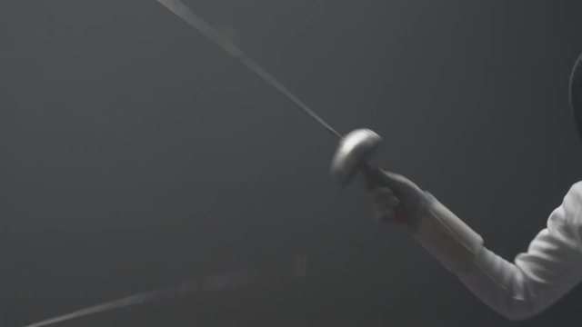 Handheld shot of a fencer practicing her parries in a dark dusty training gym