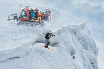 A group of freeriders arrived at the top of the mountain on a snowmobile. One skier jumps off a cliff