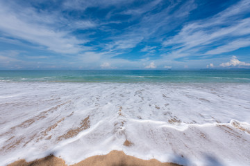 Sand beach with wave bubbles, blue sea and sky