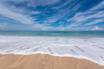 Sand beach with wave bubbles, blue sea and sky