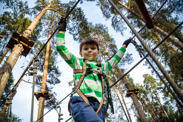 Obraz na płótnie Canvas boy climbs in a high wire park above the ground. ziplining. boy on the zip line. kid passes the rope obstacle course
