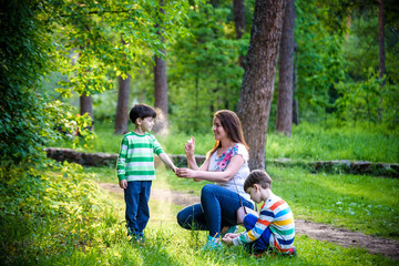 Young woman mother applying insect repellent to her two son before forest hike beautiful summer day...