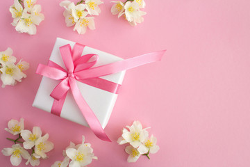 Gift with pink bow and white jasmine flowers on the pink background.Top view.Copy space.