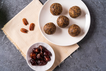 Healthy organic energy balls made with dates, oat flakes, dried cranberries, pecan nuts, in a plate on gray background.