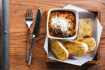 Top view of Garlic bread with meat sauce topping with mozzarella cheese, Served on wooden box with knife and fork.