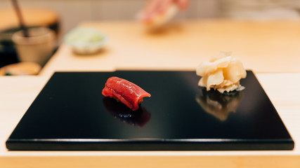 Japanese Omakase meal: Otoro (Bluefin Tuna) Sushi served by hand with pickled ginger on glossy black plate. Japanese luxury meal.
