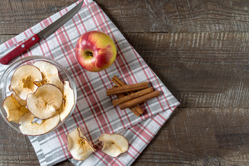 Dried apple chips , raw apple , cinnamon sticks on cooking board over wood background.