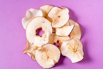 Dried apple chips over purple background with copy space.