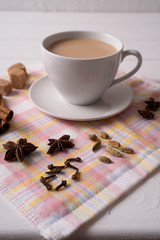 Masala chai tea in a mug and kitchen herbs, over white table background.