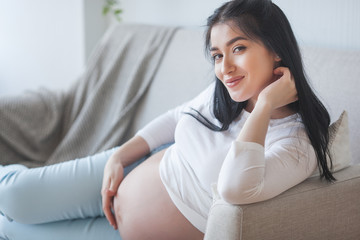 Attractive young woman expecting a child. Pregnant woman. Female indoors embracing her stomach.