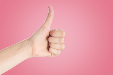 Positive gesture on a pink background. Hand show thumbs up sign, close up