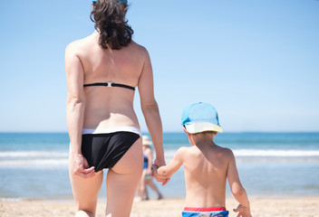 Mother with little 3 years son going to the beach, she is adjusting bikini