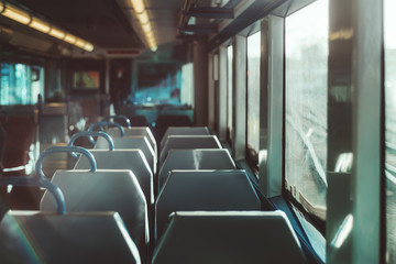 An interior of a modern empty ordinary suburban train in Europe with a row of double seats, shallow depth of field with selective focus, railroad tracks outside the window