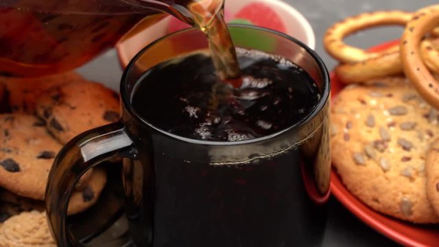 Close up of pouring tea into the black cup, cookies and marmalade