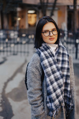 Fototapeta premium Attractive young girl wearing glasses in a coat walking on a sunny day